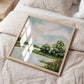 Framed landscape painting on a bed with light bedding and a side table.
