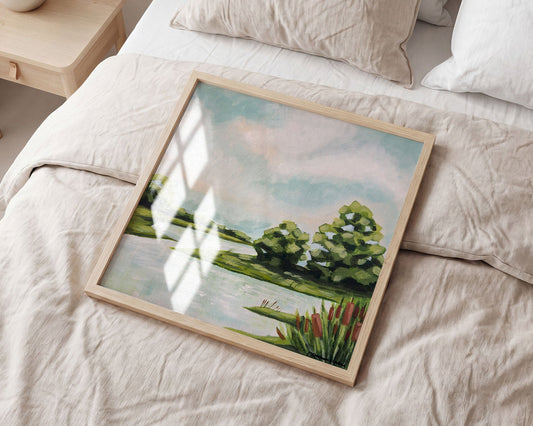 Framed landscape painting on a bed with light bedding and a side table.